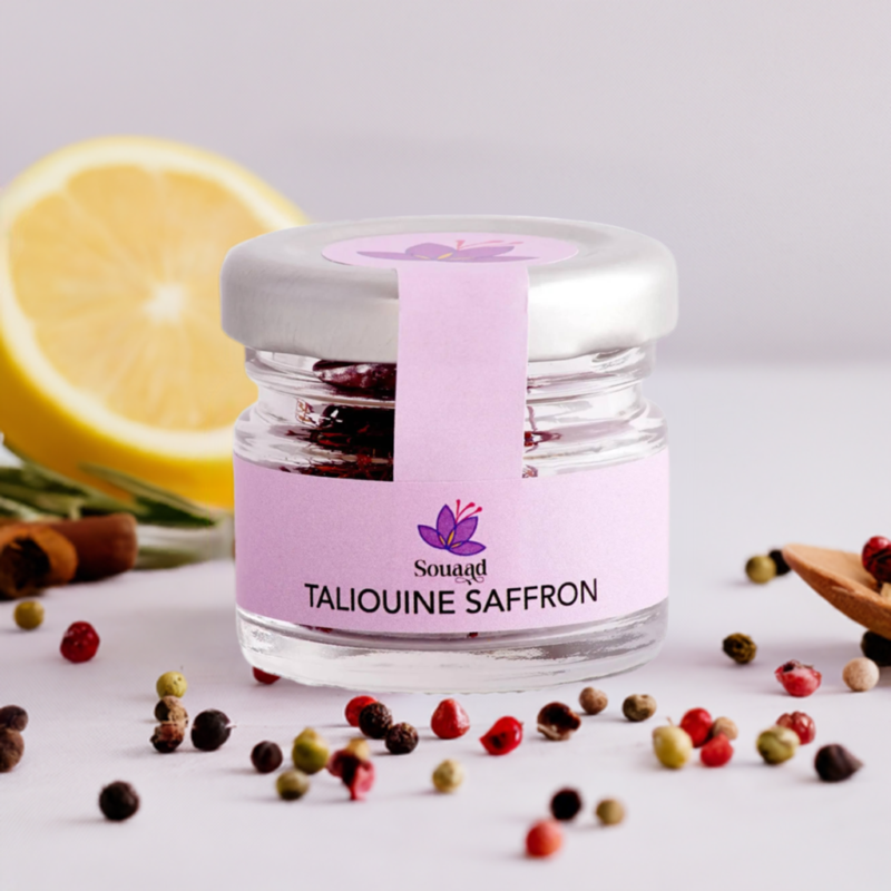 Glass jar containing 1g of Souaad's moroccan saffron set behind a few pepper corns and a lemon, highlighting the freshness of the product and its use as a spice