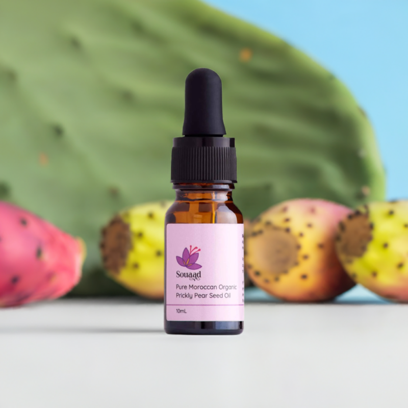 A dropper bottle of 10ml containing Souaad's prickly pear seed oil set in front of a few prickly pears showcasing the origin of the oil