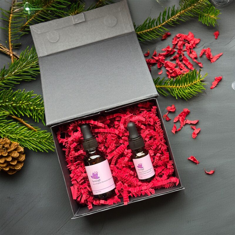 Hair oil treatment gift box wrapped in a black magnetic box with deep red crinkle paper containing one argan oil bottle and one prickly pear seed oil bottle